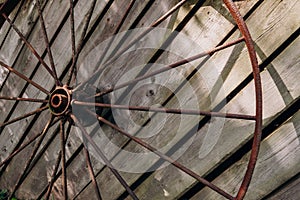 An old rusty wheel from a large cart against the background of a dilapidated unpainted fence