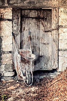 Old rusty wheelbarrow leaned against antique wooden door