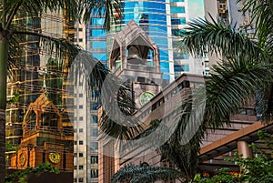 An old sandstone building with a bell tower is reflected in the windows of a glass skyscraper. Old colonial architecture and