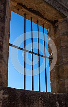 Old sandstone gaol cell jail cell with one missing window bar against blue sky