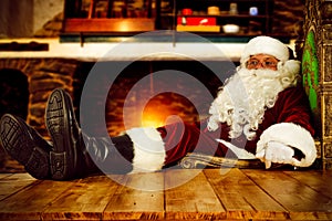 Old Santa Claus sitting in old throne chair in home interior and wooden table top with free space for your decoration.