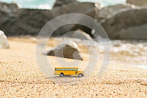 Old school bus toy on the sand of the beach. Blurred sea and stones background