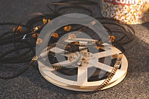 Old-school reel of uncoiled film is lying on the floor on carpet in side warm light of lamp, with caramel popcorn