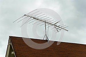 Old school television satelite on top of house or home for radio on red tiled rooftop with storm clouds in distance