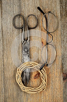 Old scissors, glasses and hank of packthread over wooden texture