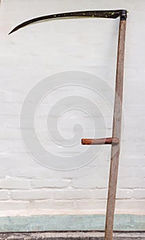 Old scythe with wooden snaith against the white wall