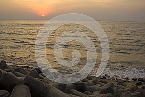 Old sea concrete embankment with tetrapods against the background of ocean waves under the bright sunset sky