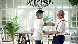 Old senior Asian couple dancing and smiling in dinner room