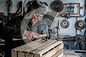 Old senior carpenter in grey warm clothes in eyeglasses