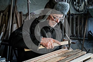 Old senior carpenter in grey warm clothes in eyeglasses