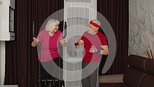 Old senior couple exercising on orbitrek, doing weight lifting sport dumbbells exercises at home