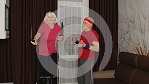 Old senior couple exercising on orbitrek, doing weight lifting sport dumbbells exercises at home