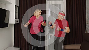 Old senior couple exercising on orbitrek, doing weight lifting sport dumbbells exercises at home