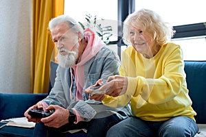 Old senior couple holding a console pad, entertaining video games playing at home