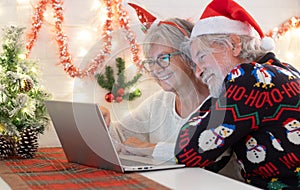 Old senior couple hugging happy in video call with family in Christmas time. Beautiful elderly caucasian family celebrating new