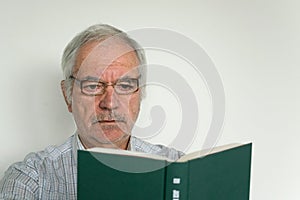 Old senior with glasses read a book closeup unhappy mad study