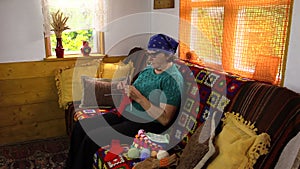 Old senior grandmother woman sit on sofa and knit stockings