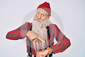 Old senior man with grey hair and long beard wearing hipster look with wool cap in hurry pointing to watch time, impatience, upset