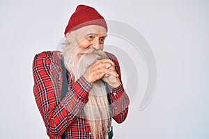 Old senior man with grey hair and long beard wearing hipster look with wool cap laughing nervous and excited with hands on chin