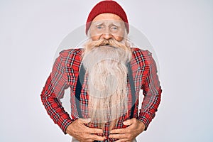 Old senior man with grey hair and long beard wearing hipster look with wool cap smiling and laughing hard out loud because funny