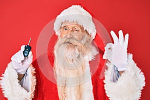 Old senior man with grey hair and long beard wearing santa claus costume holding car keys doing ok sign with fingers, smiling