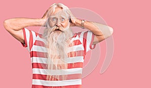 Old senior man with grey hair and long beard wearing striped tshirt crazy and scared with hands on head, afraid and surprised of