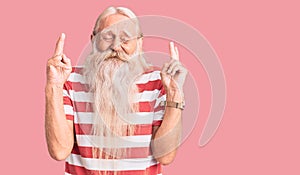 Old senior man with grey hair and long beard wearing striped tshirt gesturing finger crossed smiling with hope and eyes closed