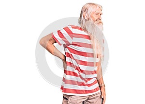 Old senior man with grey hair and long beard wearing striped tshirt suffering of backache, touching back with hand, muscular pain