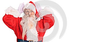 Old senior man with grey hair and long beard wearing traditional santa claus costume doing bunny ears gesture with hands palms