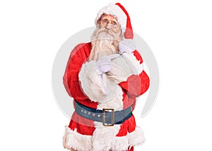 Old senior man with grey hair and long beard wearing traditional santa claus costume in hurry pointing to watch time, impatience,