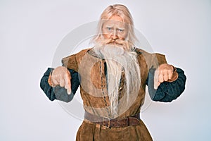 Old senior man with grey hair and long beard wearing viking traditional costume pointing down looking sad and upset, indicating