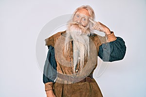 Old senior man with grey hair and long beard wearing viking traditional costume smiling pointing to head with one finger, great