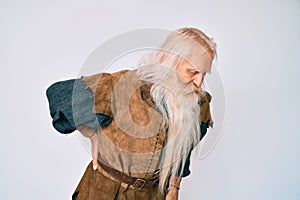 Old senior man with grey hair and long beard wearing viking traditional costume suffering of backache, touching back with hand,