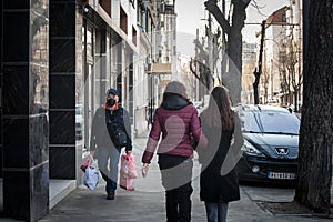 Old senior man wearing a respiratory face mask walking in the street of Belgrade with a groceries bag in winter during the covid