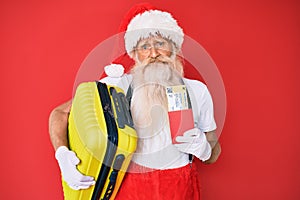 Old senior man wearing santa claus costume holding suicase and boarding pass depressed and worry for distress, crying angry and