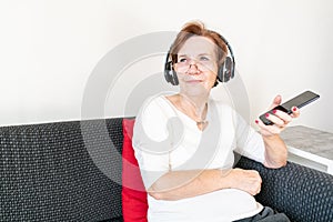 Old senior woman female sit home flat couch listen music headphones happy smile relax enjoy