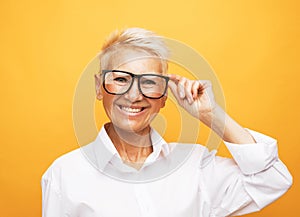 Old senior woman wear eyeglasses smiling and feeling happyness over yellow background.