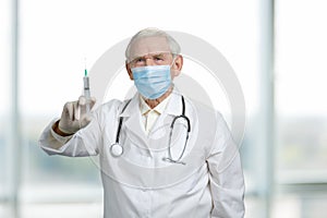 Old serious doctor holding syringe with vaccine.