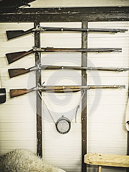 Old service rifles of British military with powder flask hanging on wooden wall. The fowling piece on a white wall