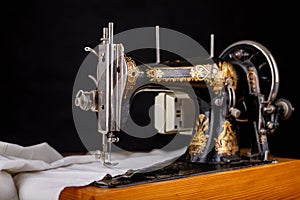 Old sewing machine and white material on a dark table. An antique device for small housework