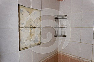 old shabby bathroom with fallen tiles. an old shelf. a piece of peeling wall