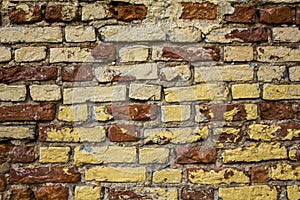 Old shabby damaged white, beige, red brick wall with yellow spots of paint closeup. rough surface texture