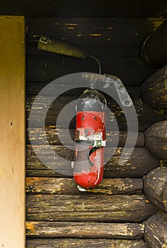An old, shabby fire extinguisher mounted on a wall of a wooden building