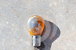 An old, shabby light bulb lies on the warm concrete, illuminated by the sun