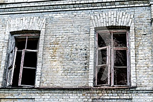 Old shabby ruined abandoned brick building wall facade with two wooden brocken glass windows and dark black background