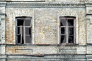 Old shabby ruined abandoned brick building wall facade with two wooden brocken glass windows and dark black background. Shattered