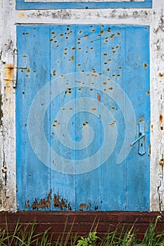 Old shabby wooden door, blue and white, with rusty hinges, a handle, a lock, and nails. Copy space.