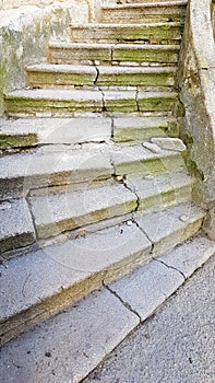 Old shattered stone stairs with deep cracks and green moss