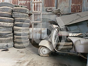 In the old shed, there are broken old motorbikes left behind,  and many old truck tires. Rusty old galvanized shed wall.