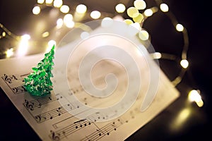 Old sheet with Christmas music notes as background against blurred lights